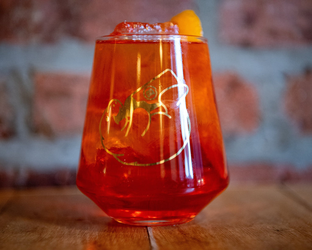 Red cocktail in a glass with a gold logo on a wooden surface
